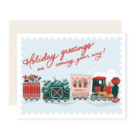 A vibrant and whimsically illustrated Christmas card featuring a festive train overflowing with colorful presents. The card's text reads 'Holiday greetings are coming your way