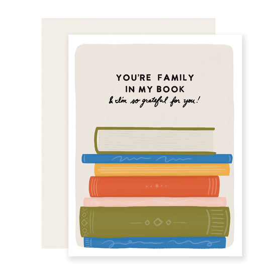 A heartfelt card that reads 'You're family in my book and I am so grateful for you.' The card features a vibrant stack of books with the message lovingly written above the books.