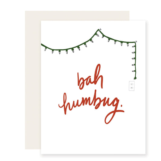  A cheeky holiday card with a minimalist design, featuring a single strand of twinkling lights draped across the top. In bold red letters, the card proclaims 'Bah Humbug,' capturing a playful, festive spirit for those with a humorous take on the season.