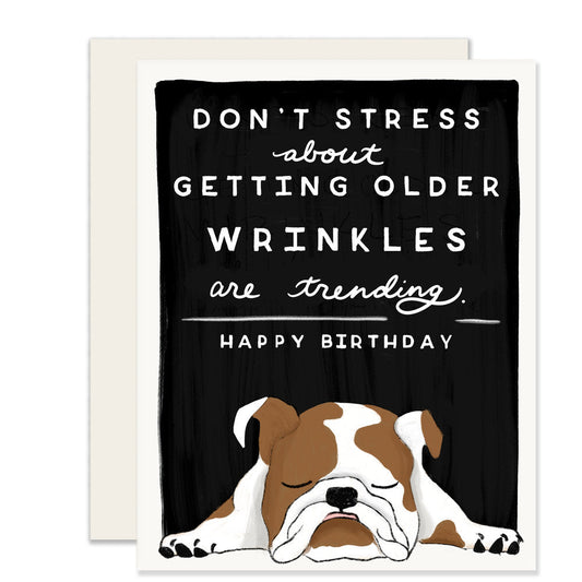 A birthday card featuring an illustration of a wrinkly bulldog and the message 'Don't stress about getting older. Wrinkles are trending. Happy Birthday.' The card adds a playful touch to the celebration, embracing the humor of aging with a lovable bulldog. 🎂🐶😄